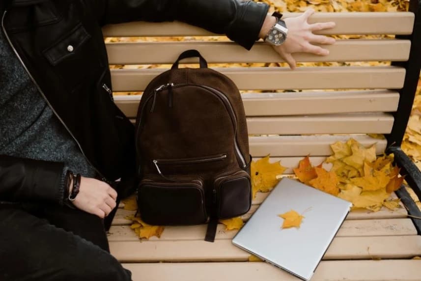 Kto stworzy program dla parku im. Stefana Żeromskiego? Osoba siedząca na ławce w parku. Obok znajduje się brązowy plecak i laptop.