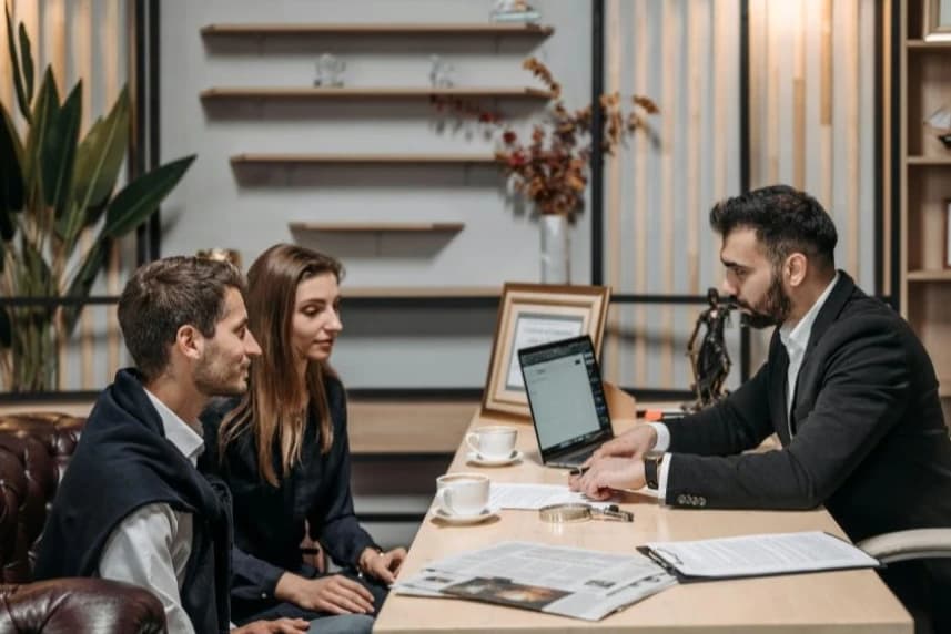 Niskie oprocentowanie, realne wsparcie. Poręczenia ARMS dla przedsiębiorców Trzy osoby przy biurku podczas spotkania biznesowego.