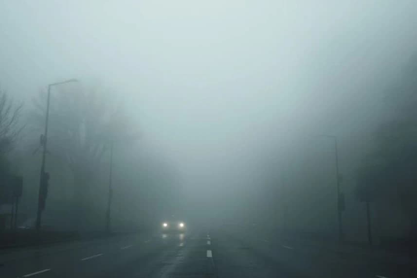 Ostrzeżenie przed wystąpieniem mgły Zamglona ulica miasta. Na zdjęciu widać światła samochodu.