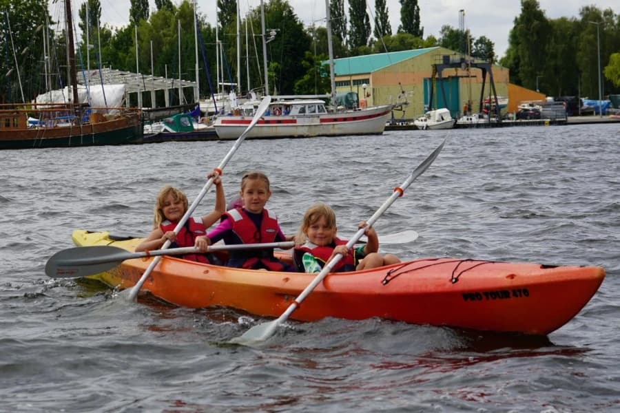 Lato pod żaglami. Letnie półkolonie w Centrum Żeglarskim Trójka dzieci w zółto-pomarańczowym kajaku.