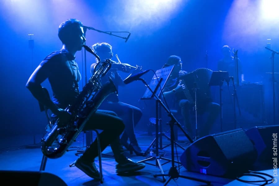 19 kwietnia TRAFO zabrzmi „Raportem z niewidzianego” Grupa muzyków podczas koncertu, w niebieskiej poświacie.