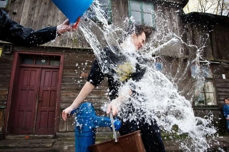 Straż Miejska przypomina: Dyngusowe lanie z umiarem! Moment wylania wody z niebieskiego wiadra na osobę przy niebieskiej pompie wodnej.