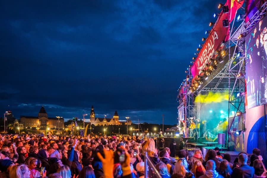 Majówka 2026 w Szczecinie. Otwieramy sezon na Łasztowni! Tłum ludzi zgromadzonych pod sceną. W tle ciemne niebo i zabytki Szczecina.