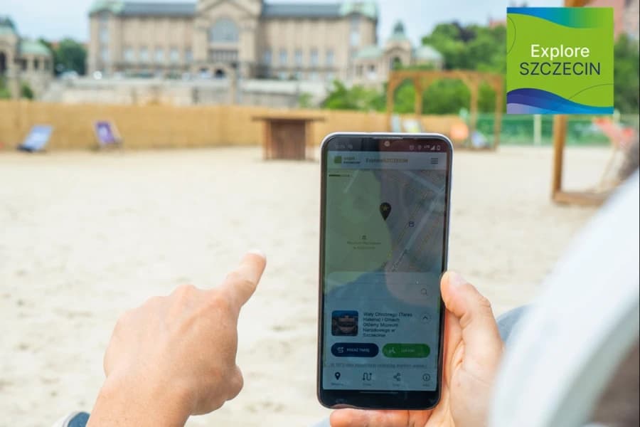 Aktywny wypoczynek w Szczecinie? Koniecznie z pomocą naszych aplikacji! Smartfon trzymany w ręku przez osobę siedzącą na plaży miejskiej.