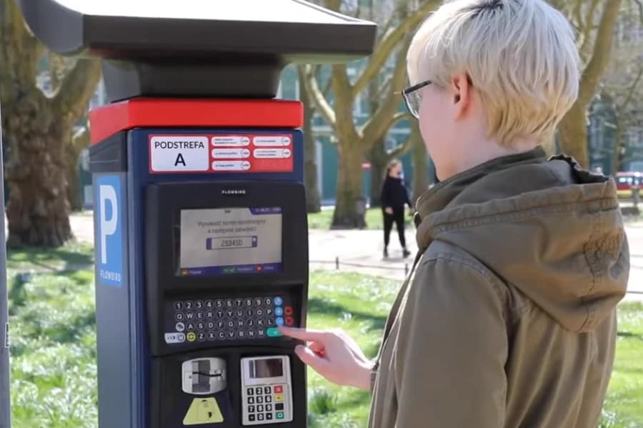 Zapraszamy do udziału w konkursie „Intuicyjny Parkomat” Osoba ubrana w kurtkę z kapturem przy parkomacie.