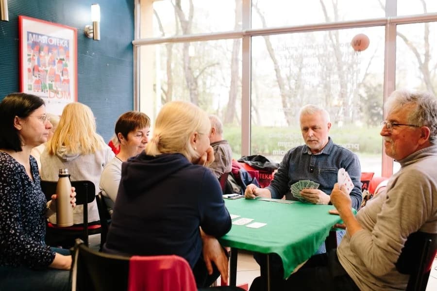 Café Przyjaźń. Przestrzeń otwarta dla mieszkańców Grupa osób siedząca przy stoliku i grająca w brydża.